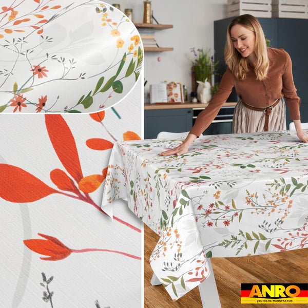 Tischdecke mit floralem Blättermuster auf einem Tisch in heller Küche. Nahaufnahme zeigt Materialstruktur. Anro Deutsche Manufaktur Logo.