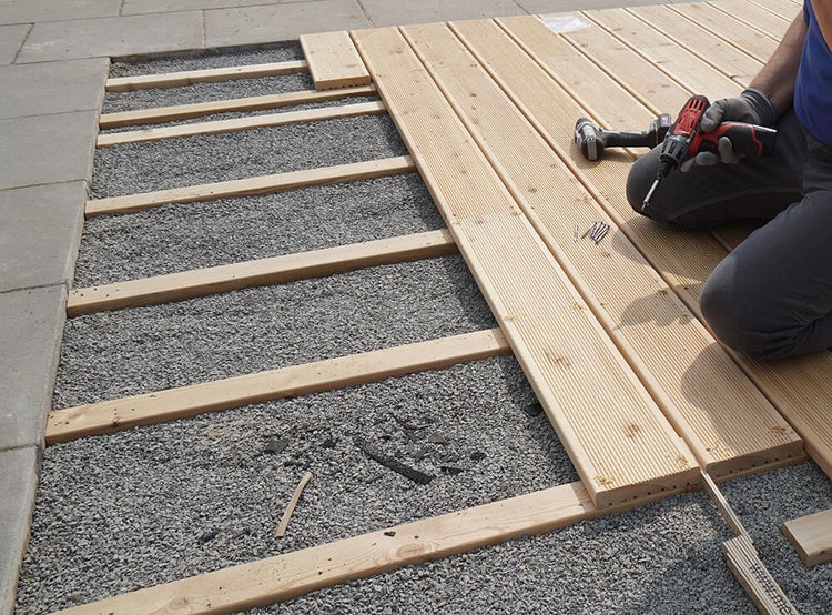 Montage von Terrassendielen auf einer Holz-Unterkonstruktion über einem Kiesbett mit einem Akkuschrauber.