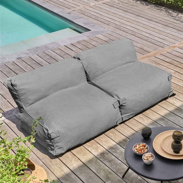 Graues Outdoor-Sitzsack-Sofa auf einer Holzterrasse neben einem Pool mit einem kleinen Tisch im Vordergrund.