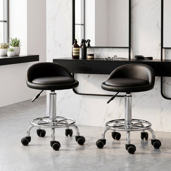 Zwei höhenverstellbare Rollhocker mit schwarzem Sitzpolster und Chromgestell in einem modernen Salon mit Marmorwand.