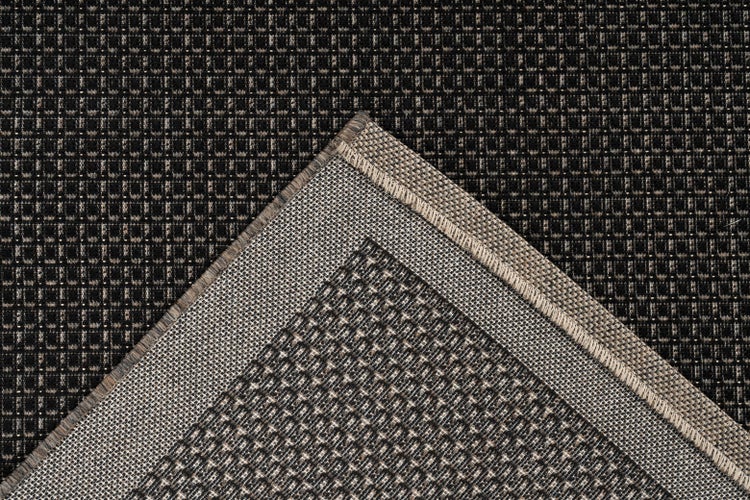 Nahaufnahme eines Teppichs mit gitterartiger Webstruktur und umgeklappter Ecke, die die Unterseite zeigt.