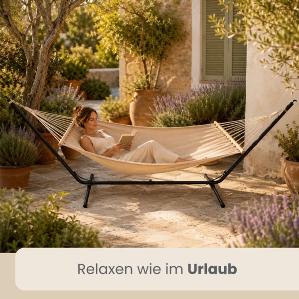Eine Frau liest ein Buch in einer Stab-Hängematte mit Metallgestell auf einer hellen, mediterranen Terrasse mit Lavendelpflanzen.