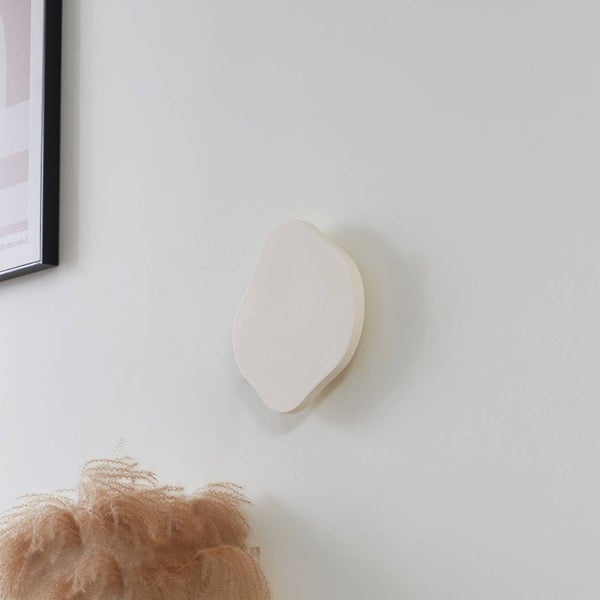 Minimalistische Wandleuchte mit organischer asymmetrischer Form in einer modernen Inneneinrichtung mit Bilderrahmen und Ziergras.