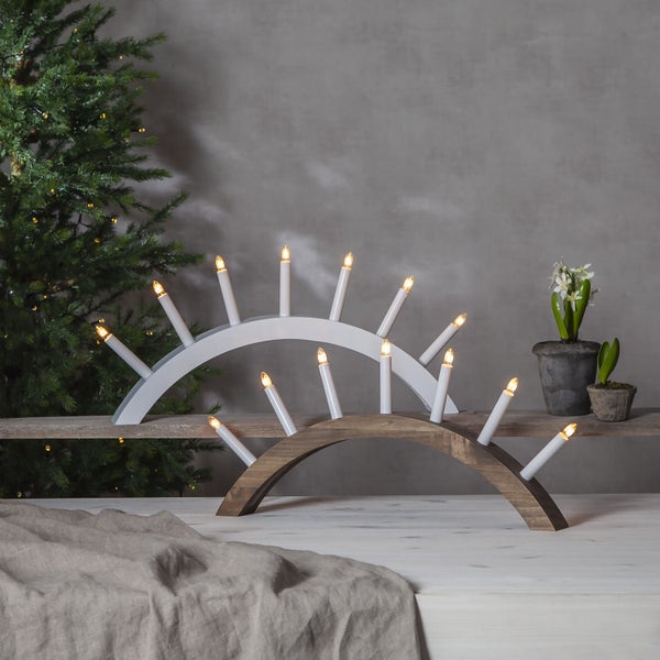 Zwei Adventsleuchter aus Holz mit Kerzenleuchten auf einem Tisch neben einem Weihnachtsbaum.