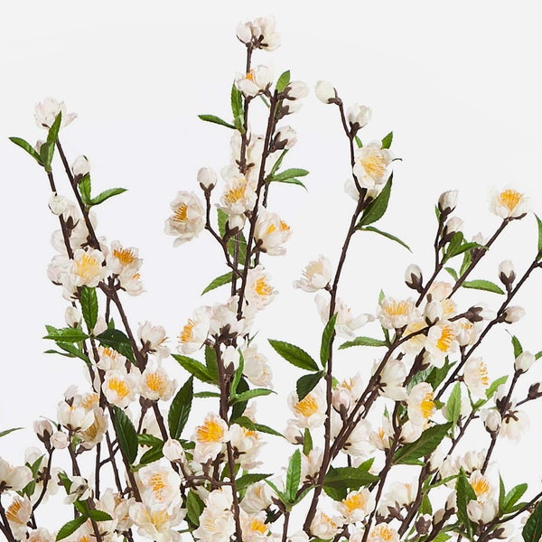 Künstlicher Kirschblütenzweig mit weißen Blüten und grünen Blättern.