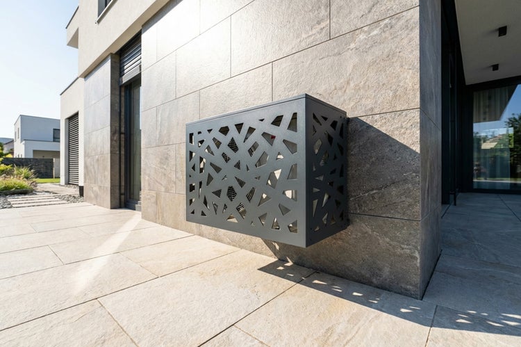 Klimaanlagen-Verkleidung aus Metall mit geometrischem Muster an einer modernen Hauswand aus Naturstein.