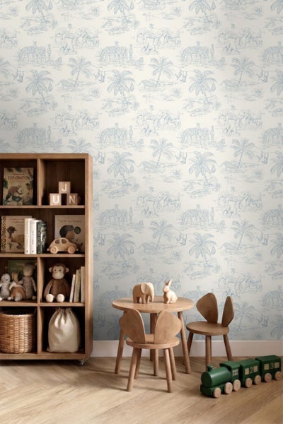 Vliestapete mit blauem Safari-Muster aus Elefanten, Zebras und Palmen in einem hellen Kinderzimmer mit Holzmöbeln und Spielzeug.