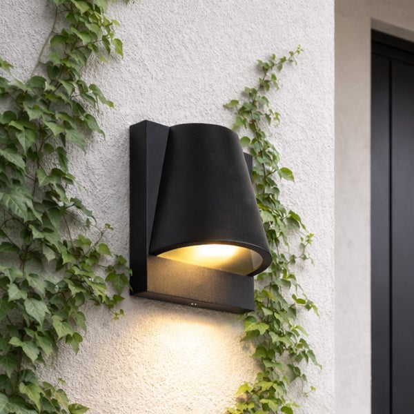 Moderne schwarze Außenwandleuchte in Kegelform an einer weißen Wand mit Kletterpflanzen, warmes Licht nach oben und unten strahlend.