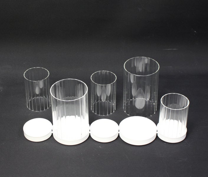 Eine Reihe von durchsichtigen Glaszylindern unterschiedlicher Größe mit dazugehörigen Deckeln.