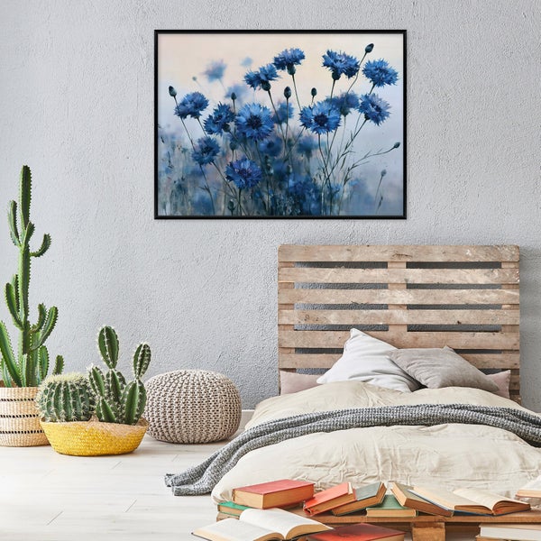 Wandbild mit blauen Kornblumen im schwarzen Rahmen über einem Bett mit Palettenkopfteil in einem Schlafzimmer mit Kakteen und Büchern.