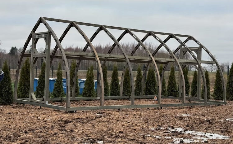 Freistehendes Gewächshaus-Gestell aus Holz mit spitz zulaufendem Bogendach im Garten.