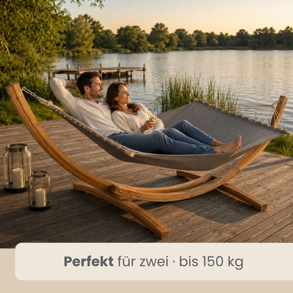 Paar in grauer Hängematte mit Holzgestell auf Holzterrasse am See bei Abendlicht, geeignet für zwei Personen bis 150 Kilogramm.