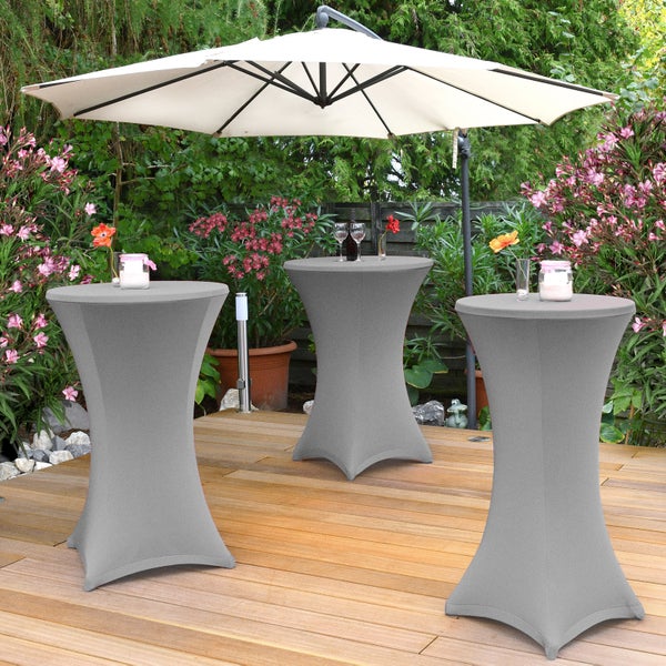 Szene im Freien mit drei Stehtischen unter einem Sonnenschirm, umgeben von Pflanzen