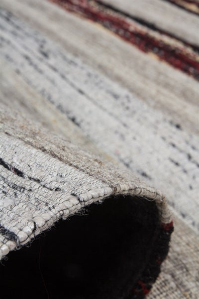 Nahaufnahme eines flachgewebten Teppichs mit Streifenmuster und sichtbarer Rückseite an der Kante.