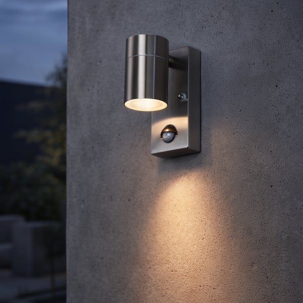 Moderne Außenwandleuchte aus Edelstahl mit Bewegungsmelder, montiert an einer Betonwand bei Dämmerung mit warmem Lichtstrahl nach unten.