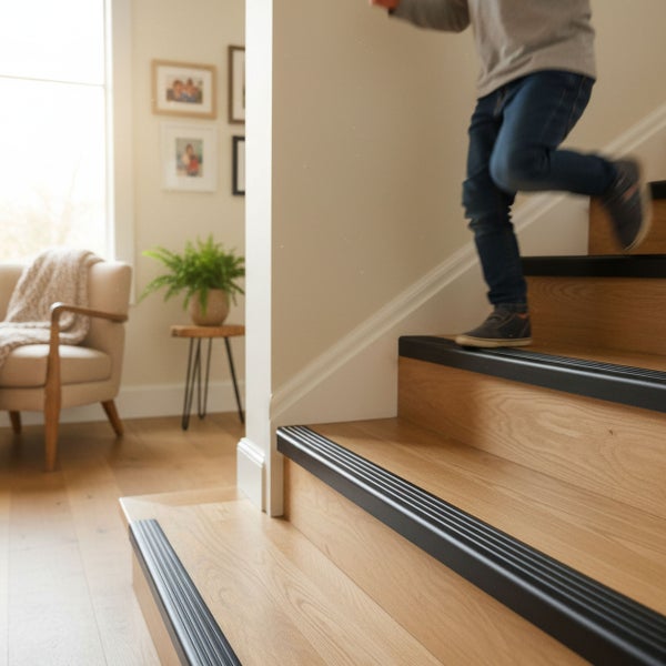 Kind läuft eine Holztreppe mit rutschfesten Treppenkantenprofilen in einem hellen Wohnraum hinunter.