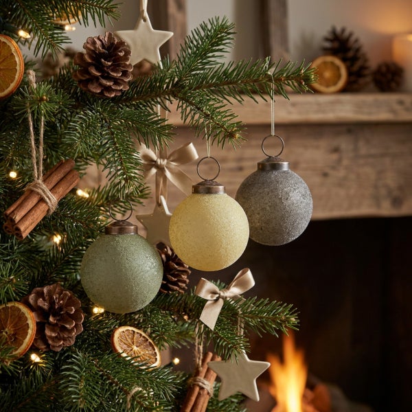 Weihnachtsbaum geschmückt mit Glas-Weihnachtskugeln, getrockneten Orangenscheiben, Zimtstangen und Sternanhängern vor einem Kamin.