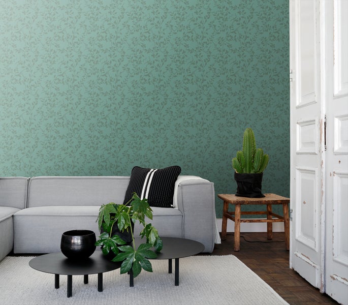 Wohnzimmer mit floral gemusterter Tapete, Sofa, Tisch und Zimmerpflanzen