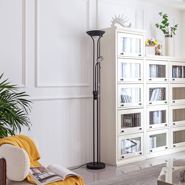 Schwarze Stehleuchte mit Deckenfluter und verstellbarem Lesearm in einem hellen Wohnzimmer neben einem weißen Bücherregal.