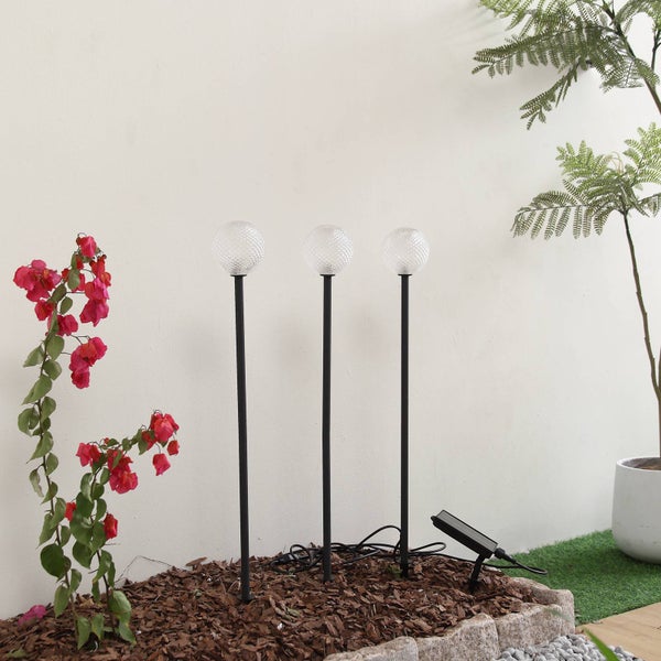 Drei Solar-Gartenleuchten in Kugelform mit strukturierter Oberfläche auf schwarzen Erdspießen inklusive externem Solarmodul in einem Beet.