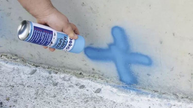 Eine Hand sprüht Markierspray auf eine Betonoberfläche.