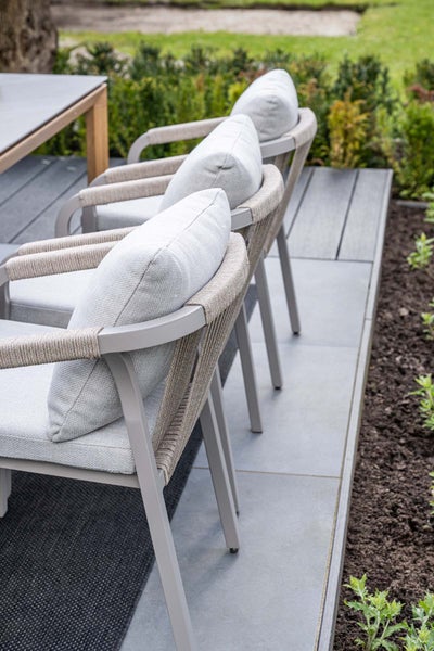 Moderne Gartenstühle mit Seilgeflecht am Rücken und grauen Sitzkissen auf einer Terrasse neben einem Esstisch.