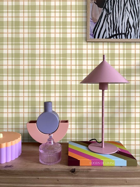 Dekorative Wohnelemente auf einem Holzmöbelstück vor einer Wand mit Karomuster.