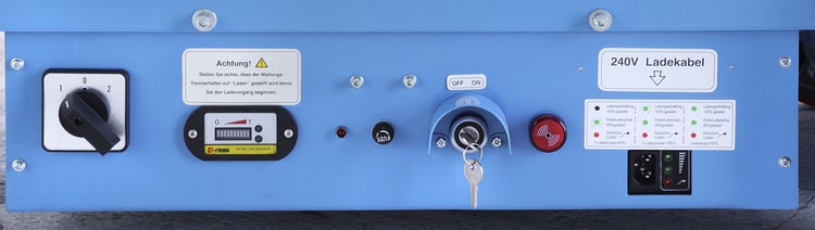 Detailansicht einer blauen Steuerungseinheit mit Schaltern, Anzeigen und Warnhinweisen