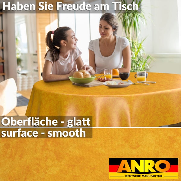 Glatte, gelb-orange gemusterte Tischdecke auf einem runden Tisch in einem hellen Esszimmer. Mutter und Kind beim Frühstück. ANRO Logo.