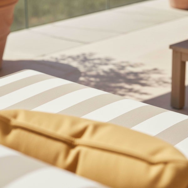 Nahaufnahme von gestreiften und einfarbigen Outdoorkissen auf einer hellen, sonnigen Terrasse.