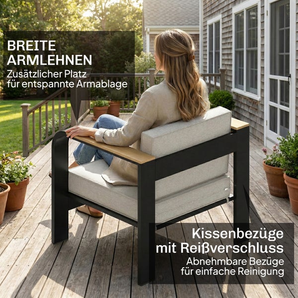 Garten-Loungesessel mit schwarzem Rahmen, breiten Holz-Armlehnen und grauen Kissen auf einer Terrasse. Abnehmbare Kissenbezüge mit Reißverschluss.
