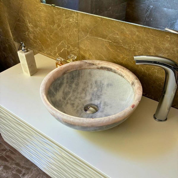 Modernes Badezimmer mit einem runden Aufsatzwaschbecken aus Naturstein auf einem weißen Unterschrank mit Wellenstruktur und einer Chromarmatur.