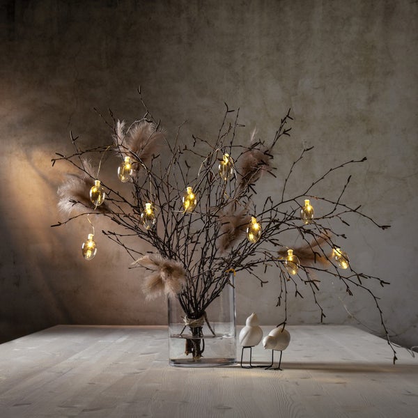 Dekorative Äste mit Federn und Lichterkette in einer Vase, mit zwei kleinen Vogel Dekorationen auf einem Tisch