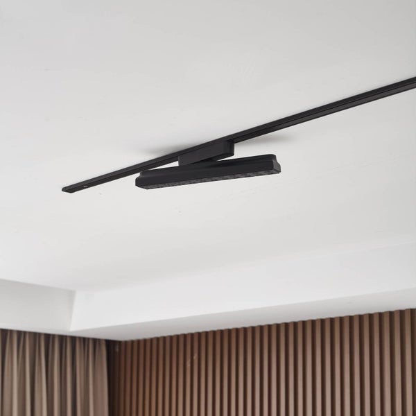 Schwarzer LED-Strahler an einem Schienensystem an einer weißen Zimmerdecke in einem modernen Raum mit Holzpaneelen.