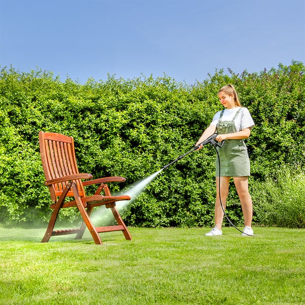 Eine Hand befüllt einen weißen Sprühbehälter mit blauer Flüssigkeit aus einer Flasche auf einer gepflasterten Außenfläche im Garten.