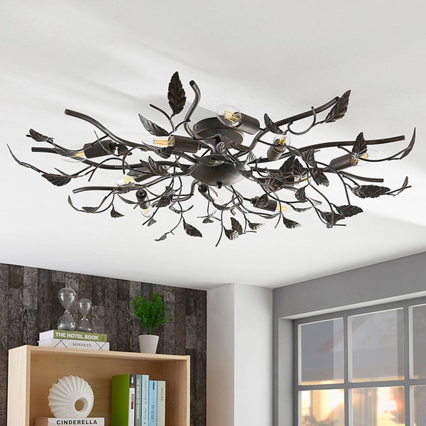 Dekorative Deckenleuchte aus Metall in Ast-Optik mit Blättern, montiert an einer Decke in einem hellen Raum mit Bücherregal.