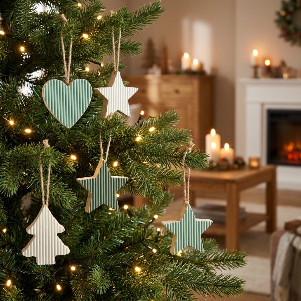 Weihnachtsbaumschmuck aus Holz in Herz Stern und Tannenbaum Form hängend am Tannenbaum in einem gemütlich eingerichteten Wohnzimmer