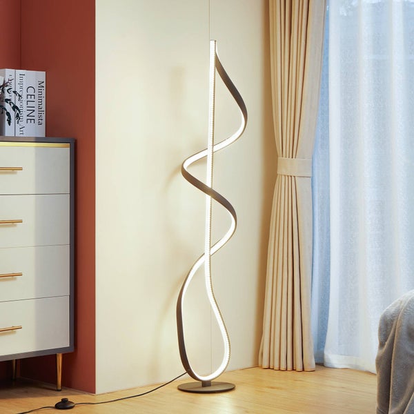 Moderne LED-Stehleuchte in Spiralform aus Metall mit integriertem Leuchtmittel in einem hellen Wohnraum. Die Leuchte steht auf einem Holzboden.