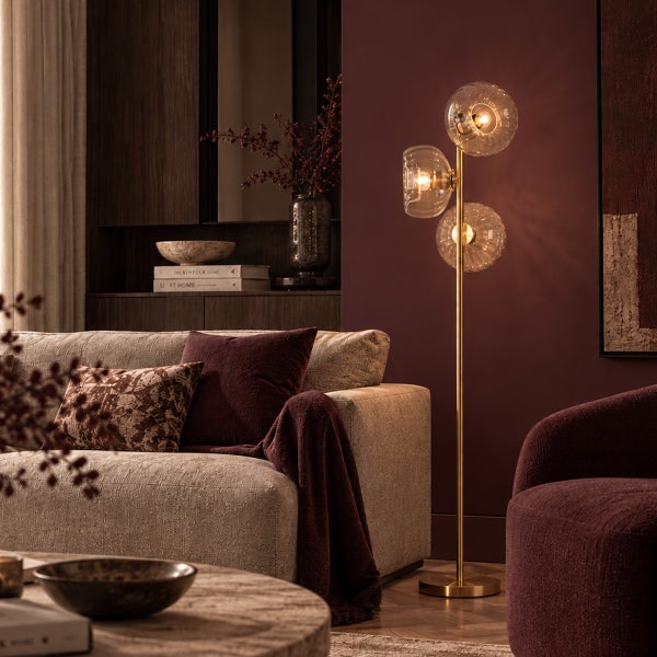 Moderne Stehlampe mit drei Glaskugeln in einem stilvollen Wohnzimmer mit Sofa und dekorativen Accessoires.