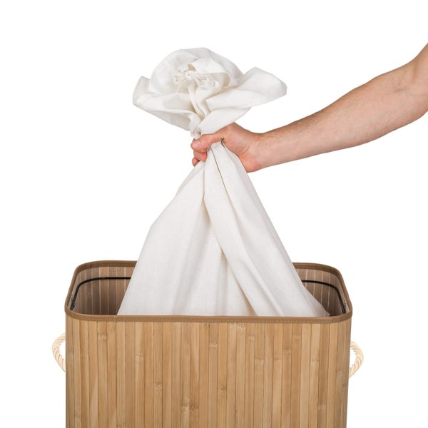 Wäschekorb aus Bambus mit einem Sack Wäsche, der von einer Hand gehalten wird