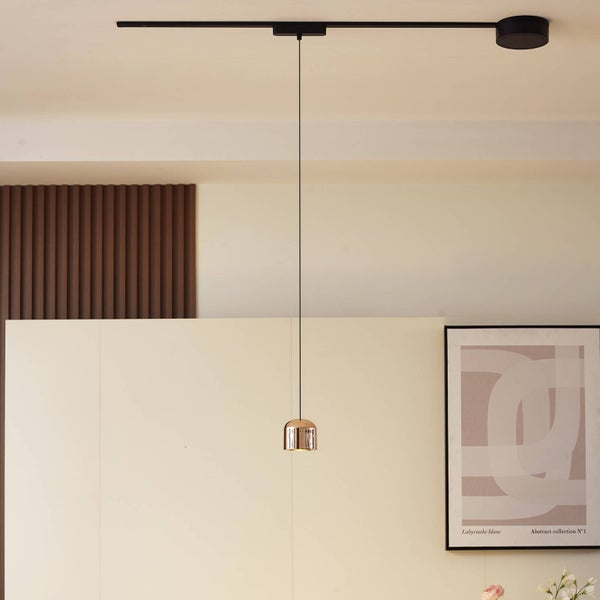 Moderne Pendelleuchte mit kupferfarbenem Glasschirm an schwarzem Schienensystem in einem hell eingerichteten Raum.