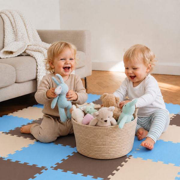 Zwei kleine Kinder spielen auf einer Spielmatte aus Schaumstoff mit einem Korb voller Plüschtiere im Wohnzimmer.