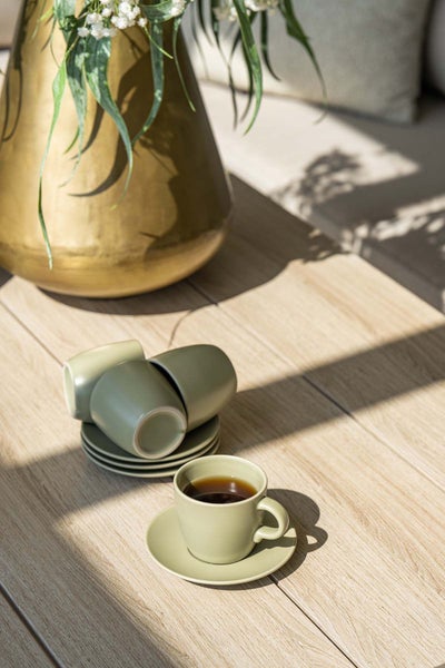 Keramische Espressotassen auf einem Holztisch im Außenbereich, eine Tasse mit Kaffee gefüllt, neben einer großen Vase mit Pflanzen.