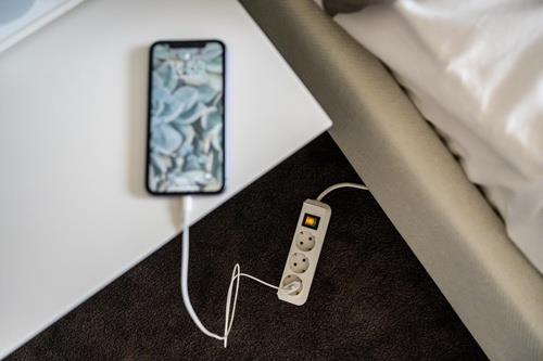 Telefon, das an einer Steckdosenleiste auf einem Nachttisch aufgeladen wird.