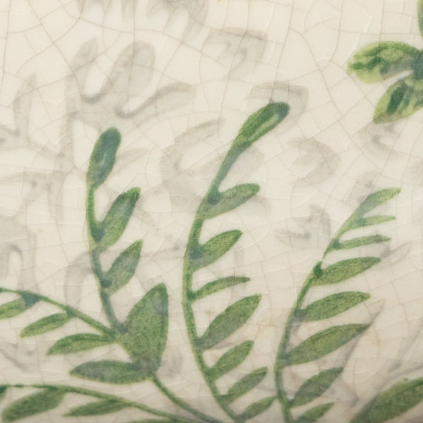 Detailaufnahme einer Keramikoberfläche mit Craquelé-Effekt und grünem Blattmuster.