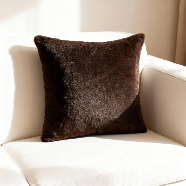 Quadratisches Dekokissen aus braunem Kunstfell auf einem hellen Sofa.