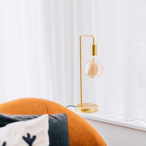 Goldene Tischleuchte mit dekorativer Glühbirne neben einem Sessel
