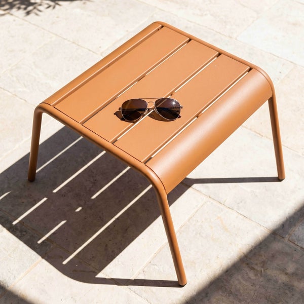 Kleiner Beistelltisch aus Metall mit Lamellenoberfläche auf einer Steinterrasse, auf dem eine Sonnenbrille liegt.