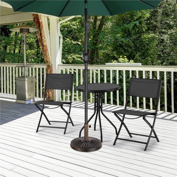 Gartenmöbel-Set auf einer Holzterrasse mit zwei schwarzen Klappstühlen, einem runden Metalltisch und einem großen grünen Sonnenschirm.