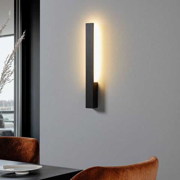Moderne schwarze LED-Wandleuchte in schmalem Design an einer Wand montiert mit warmweißem indirektem Licht in einem Wohnraum.